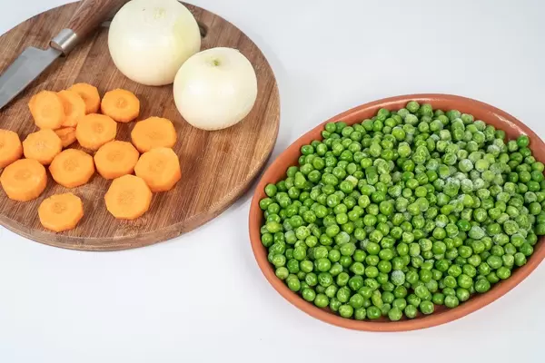 Geschnittene Möhren, Tiefkühl-Erbsen und Zwiebeln auf einem Küchentisch vor dem Kochen