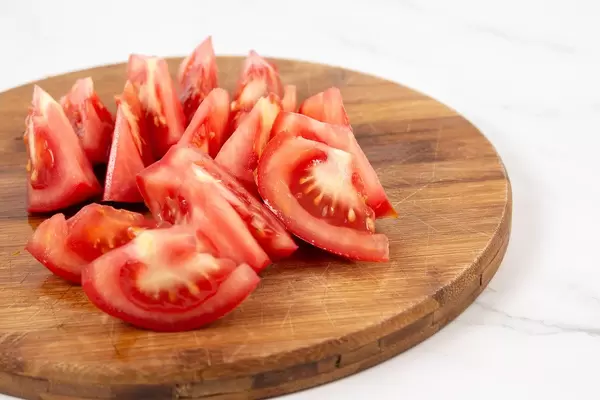 Geschnittene Tomatenstückchen auf einem runden Holzbrettchen
