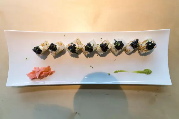 Geschnittener Sushi "Lucky No Fish", aufgereiht auf einem länglichen Teller, mit veganem Kaviar Topping, veganem Thunfischersatz und Frühlingszwiebeln,