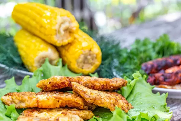 Geschnittenes Fleisch, knackige Maiskolben und Würstchen, mit Salat, sind für ein Barbecue auf dem Gartentisch angerichtet