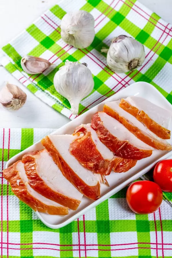 Geschnittenes und geräuchertes Hühnerfilet mit Kirschtomaten und Knoblauch auf grün-weiß-roten Geschirrtüchern