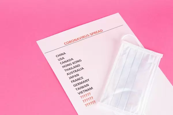 Gesichtsmaske liegt auf Liste mit Coronavirus betroffenen Ländern auf pinkem Hintergrund