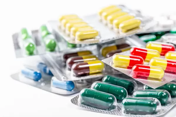 Gestapelte Verpackungen mit verschiedenen Kapseln und Tabletten auf weißem Untergrund