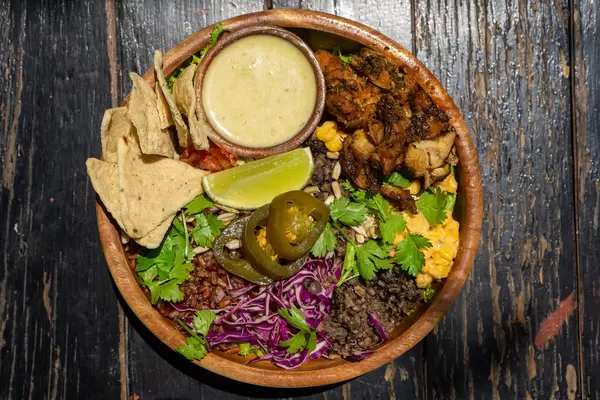 Gesunde Bowl mit Gegrilltem Hähnchen, Braunen Reis, Mais, Rotkohl, Tortilla Chips, Jalapeno Chilis, Kräutern und Soße in einer Holzschüssel von oben auf einem Holztisch fotografiert