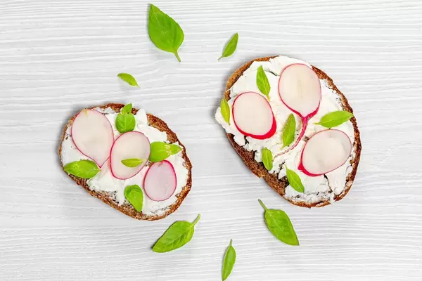 Gesunde, vegetarische Sandwiches mit Frischkäse, Radieschen und Basilikumblätter auf einem Holztisch in obene Aufnahme