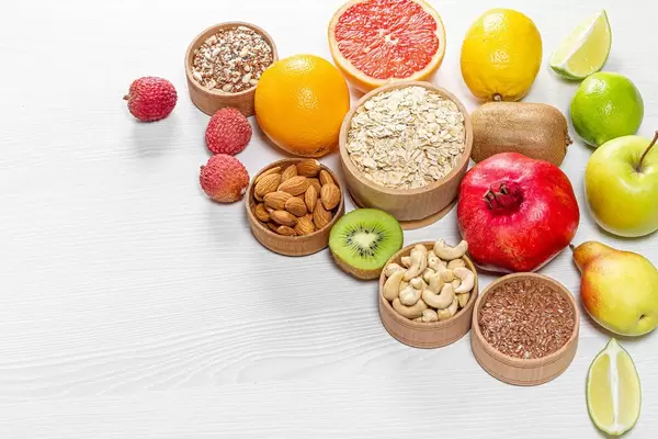 Gesunde Zutaten für ein ausgewogenes Frühstück: Obst, Nüsse und Kerne auf einem weißen Holztisch