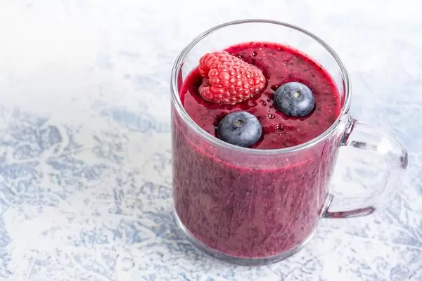Gesunder, frisch gepresster, dickflüssiger Saft oder Smoothie aus Blaubeeren und Himbeeren in Glas