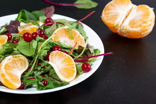 Gesunder vegetarischer Salat mit Spinat, Mandarine und Moosbeeren auf weißem Teler