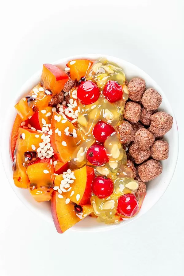 Gesundes Essen mit Maisbällchen, Tamarillo Scheiben, Kiwano Horngurke Fruchtfleisch, Sesam, Rote Johannisbeeren und andere Früchte in einer weißen Schale von oben fotografiert Hochformat