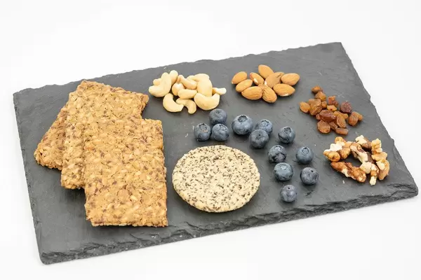 Gesundes Essen und Snacks liegen auf einem Schieferstein, wie Vollkorn-Knäckebrot, Heidelbeeren, Nüsse, Rosinen & Plätzchen mit Chia