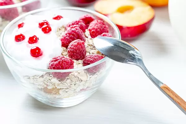 Gesundes Frühstück: Frisches Müsli mit Himbeeren und Johannisbeeren in einer Glas-Schüssel mit Löffel