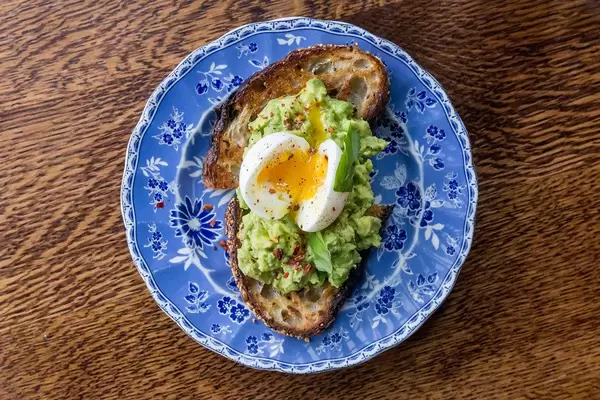Gesundes Frühstück: Mehrkornbrot-Toast mit Avocado, Ei, Lime, Chili auf einem Retro-Chic Teller, Aufnahme von oben