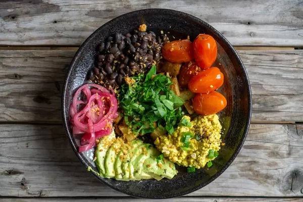Gesundes Frühstück mit Rührei, Avocado, Kirschtomaten, Bohnen und Bratkartoffeln von oben auf einem Holztisch fotografiert