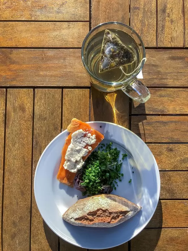 Gesundes Mittagessen, mit einem Stück Räucherlachs mit weißer Creme, grünem Salat und ein Brötchen, neben einem Glas Tee mit dreieckigem Teebeutel