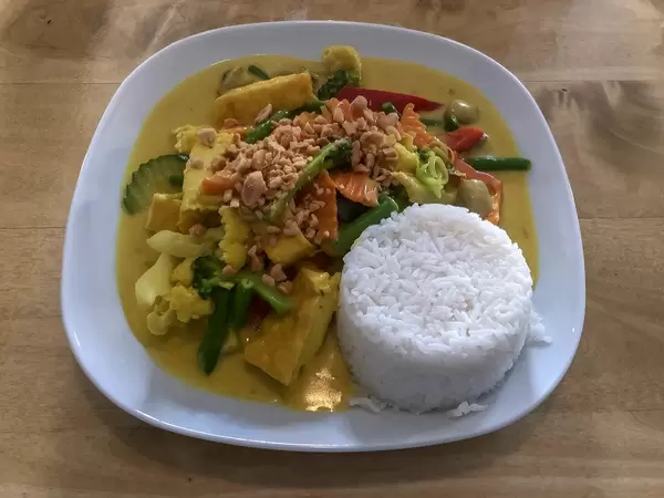 Gesundes Mittagessen mit Kurkuma Curry, Gemüse und weißem Reis, angerichtet auf einem weißen Teller