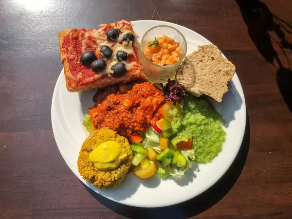Gesundes Mittagessen mit Olivenpizza, Couscous-Curry, Weißbrot und Obstsalat auf einem weißen Teller