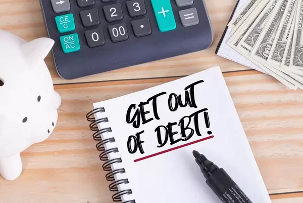 Get out of debt text in notebook with piggy bank and calculator on wooden table