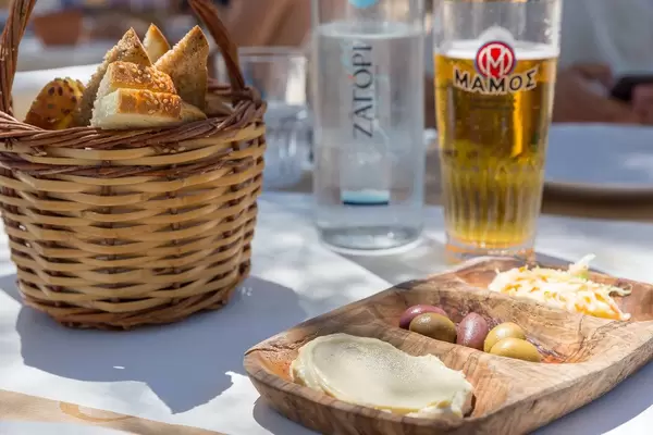 Getränke und ein Brotkorb, neben mediterranem Essen, wie Humus und Oliven, in einem griechischen Restaurant auf Paros