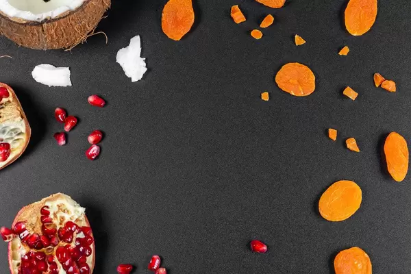 Getrocknete Aprikosen, Granatapfel und Kokosnuss von oben fotografiert auf schwarzem Hintergrund mit freier Fläche
