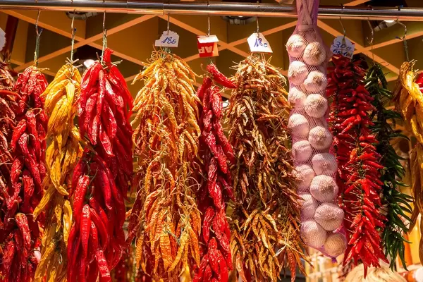 Getrocknete Gewürze wie Knoblauch, gelbe und grüne Chilischoten hängen in der Mercat de la Boqueria in Barcelona, Spanien, aus