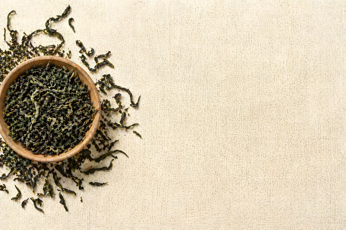 Getrocknete Teeblätter in Holzschale auf Leinenstoff