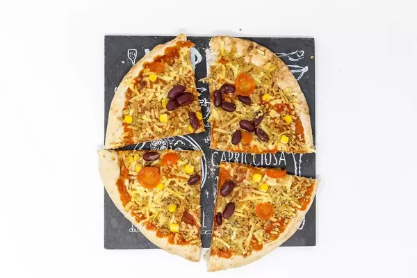 Geviertelte, fleischlose Pizza California mit roten Bohnen und Maiskörnern auf schwarzer Steinplatte