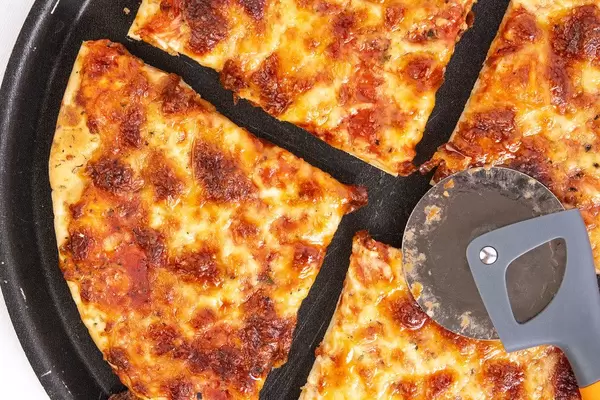 Geviertelte Margherita-Pizza mit einem Pizzaschneider / Pizzaroller