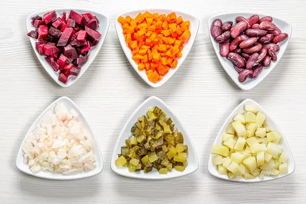 Gewürfelte Zutaten in Dreiecksschalen auf weißem Holzhintergrund