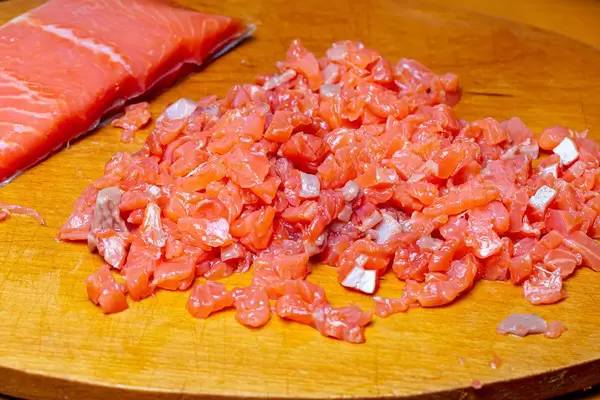 Gewürfelter Lachs neben einem Lachsfilet auf einem Holzschneidebrett