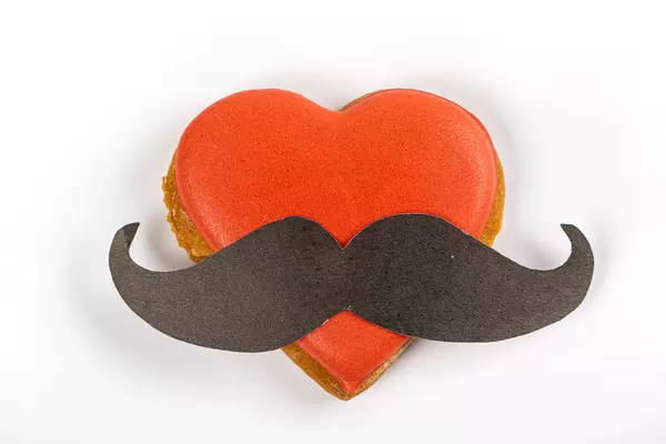 Gingerbread valentine heart with red icing and black mustache on white background