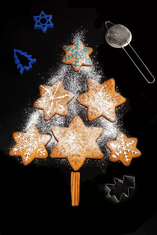 Gingerbread xmas tree with cookie cutters and strainer on black