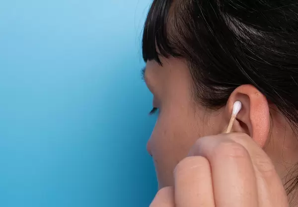 Girl cleaning her ear with a cotton swab on blue background