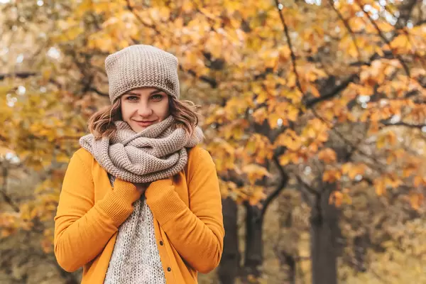Girl in a knitted hat and scarf on a background of autumn trees