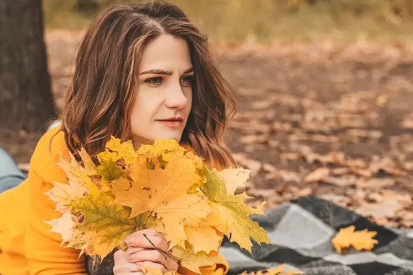 Girl in a yellow cardigan with autumn leaves resting in the park
