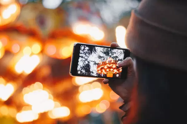 Girl taking picture with smartphone of lunapark. Colorful blurry background.