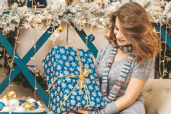 Girl with a gift on the background of a decorated room with garlands, branches of a christmas tree and decor