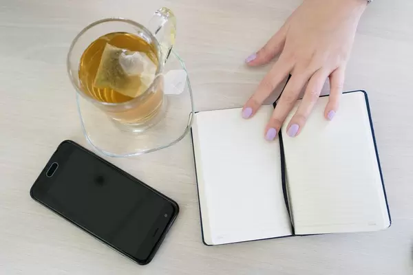 Girl's Hand Holding the Notebook on the Table