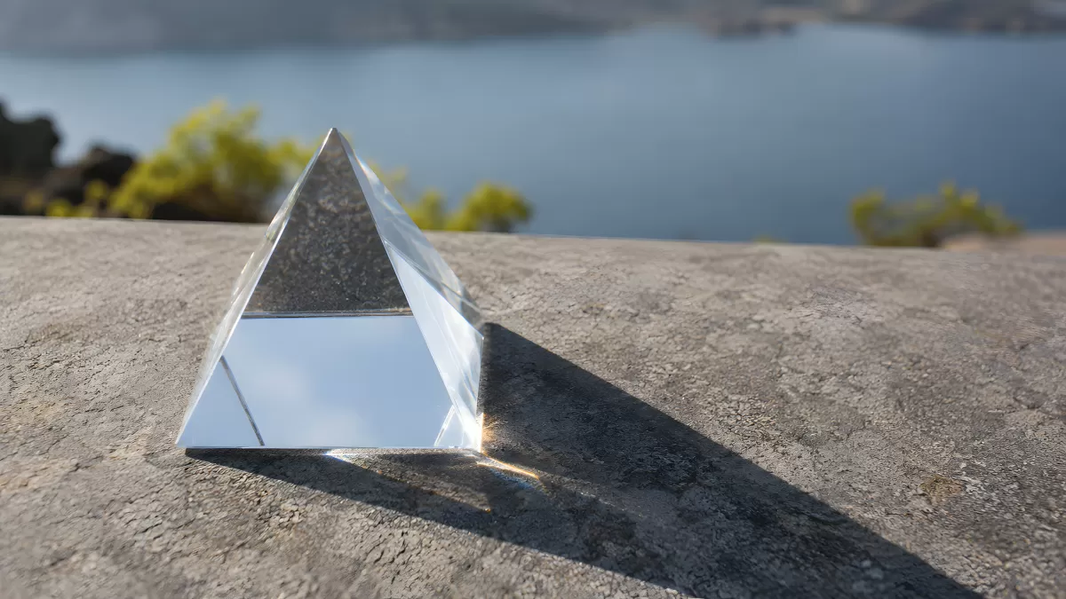 Gläserne Kristallpyramide auf Fels mit Seepanorama
