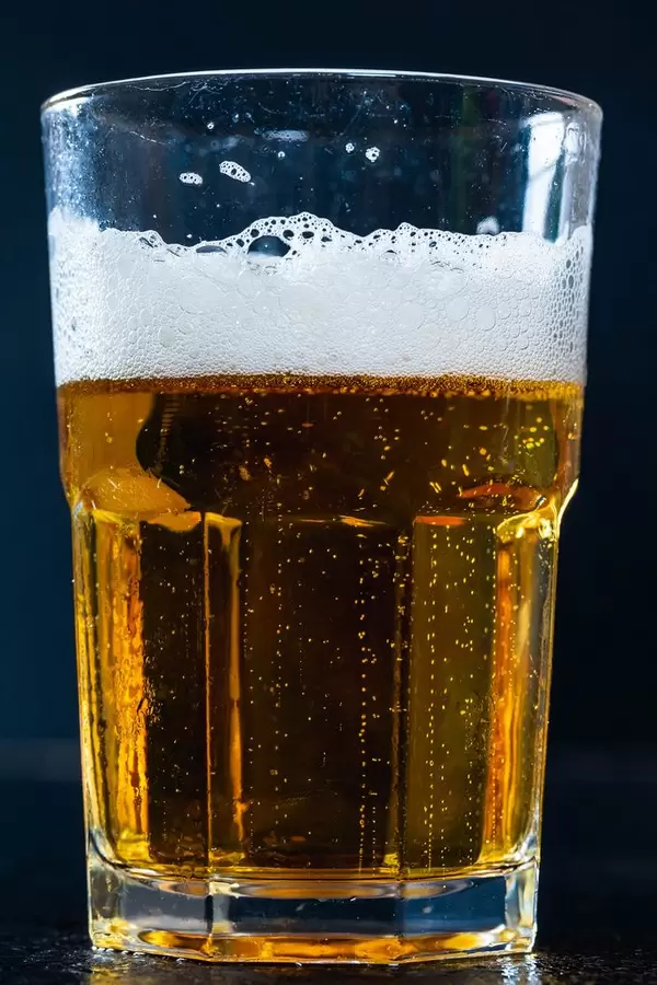 Glas mit Leichtbier und Bierschaum, nicht mehr ganz voll vor dunklem Hintergrund