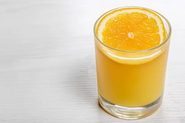 Glas mit orangen Saft und einer Scheibe Orange auf einem weißen Holzhintergrund