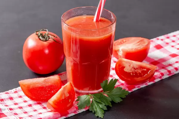 Glas mit organischem Tomatensaft, angerichtet mit ganzer Tomate, Tomatenschnitzen und Petersilie