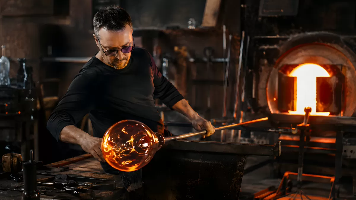 Glasbläser formt glühende Glaskugel in der Werkstatt