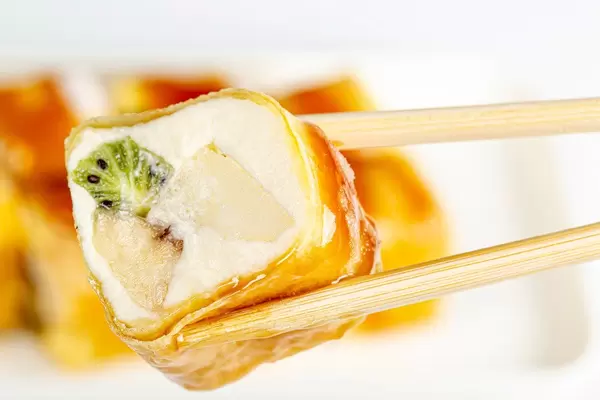 Glasierte Käsekuchen-Rolle mit Früchten zwischen Essstäbchen Nahaufnahme