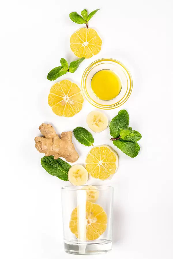 Glass and ingredients for a drink - honey, banana, lemon and ginger root on white, top view