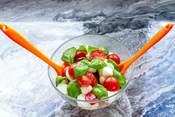 Glass bowl full of salad with two spoons for mixing ingredients (Flip 2019) (Flip 2019)