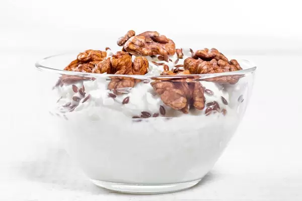 Glass bowl with cottage cheese, nuts and flax seeds on white wooden background