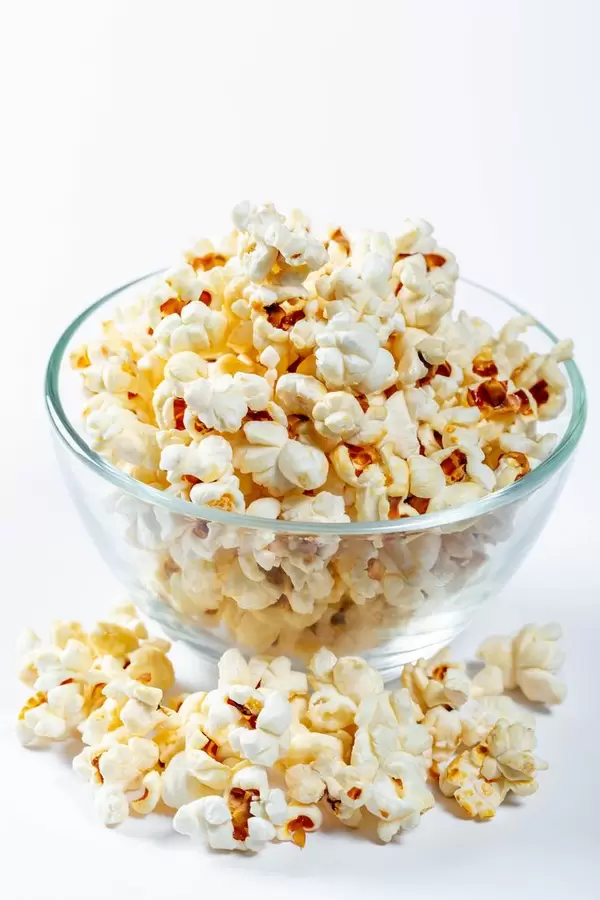 Glass bowl with popcorn on white background