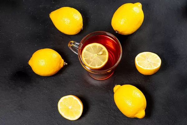 Glass Cup with black tea surrounded by fresh ripe lemons on a black background (Flip 2019)