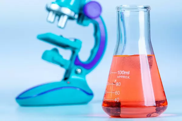 Glass flasks with red solution with a microscope in the background