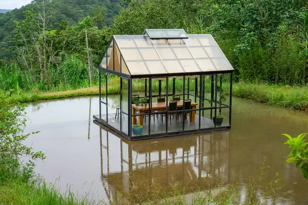 Glass House with Table and Chairs in the Middle of a Pond within Nature